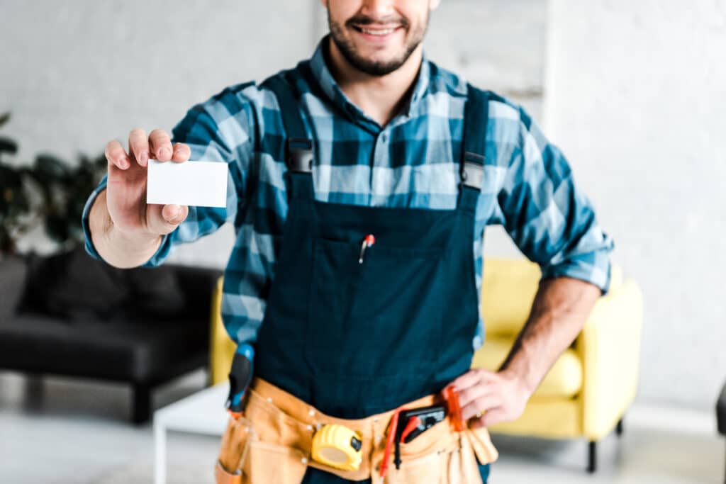 cropped view of cheerful worker holding blank card and standing with hand on hip